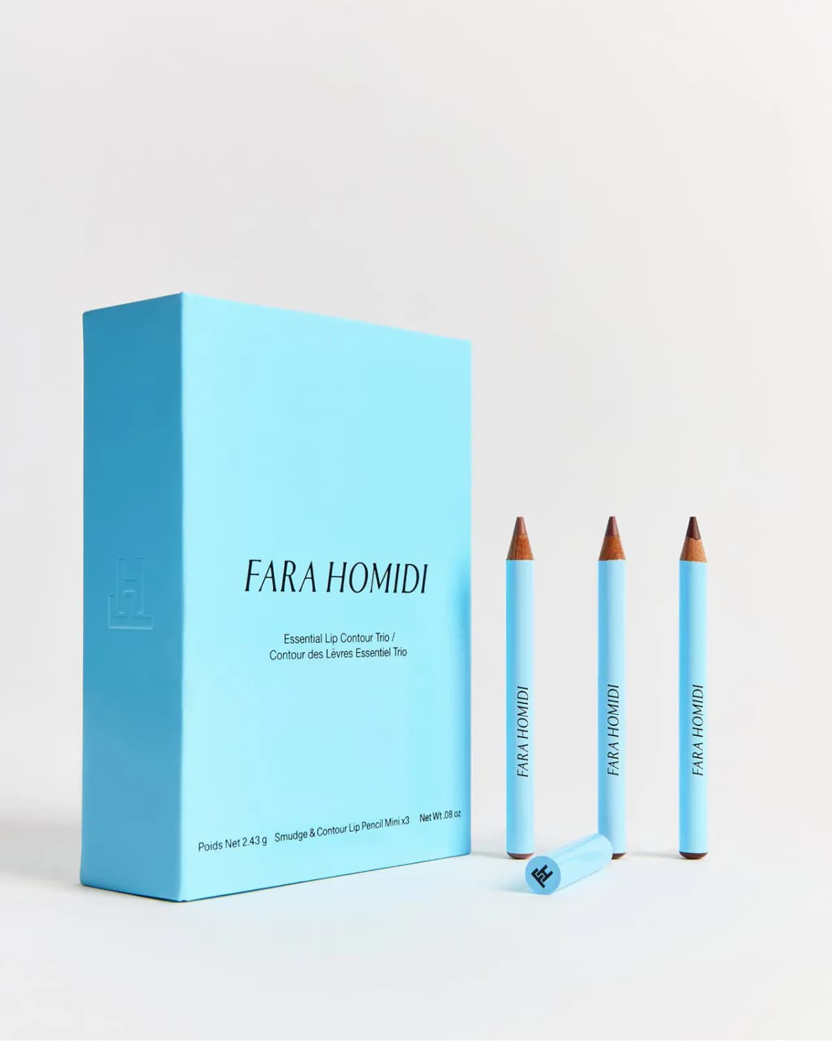 Closed sky-blue Fara Homidi Essential Lip Contour Trio box beside three sharpened mini pencils and a cap