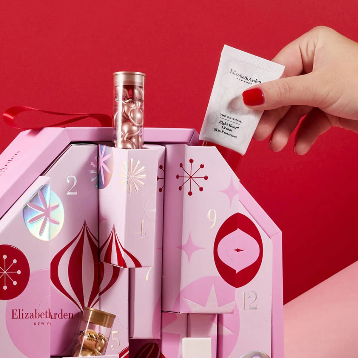 Hand with red nails pulling Eight Hour Cream from the pink calendar beside a tube of pink ceramide capsules.