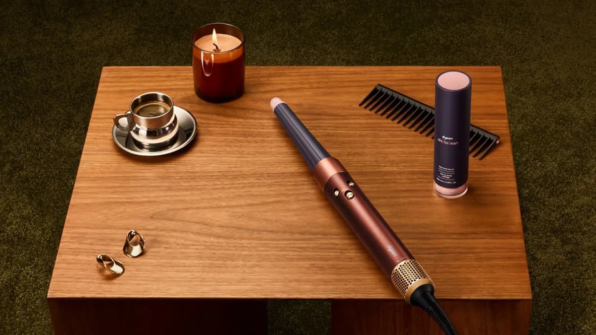 Plum and copper multi-styler with conical barrel on a walnut table beside Dyson chi|to|san serum, candle and espresso