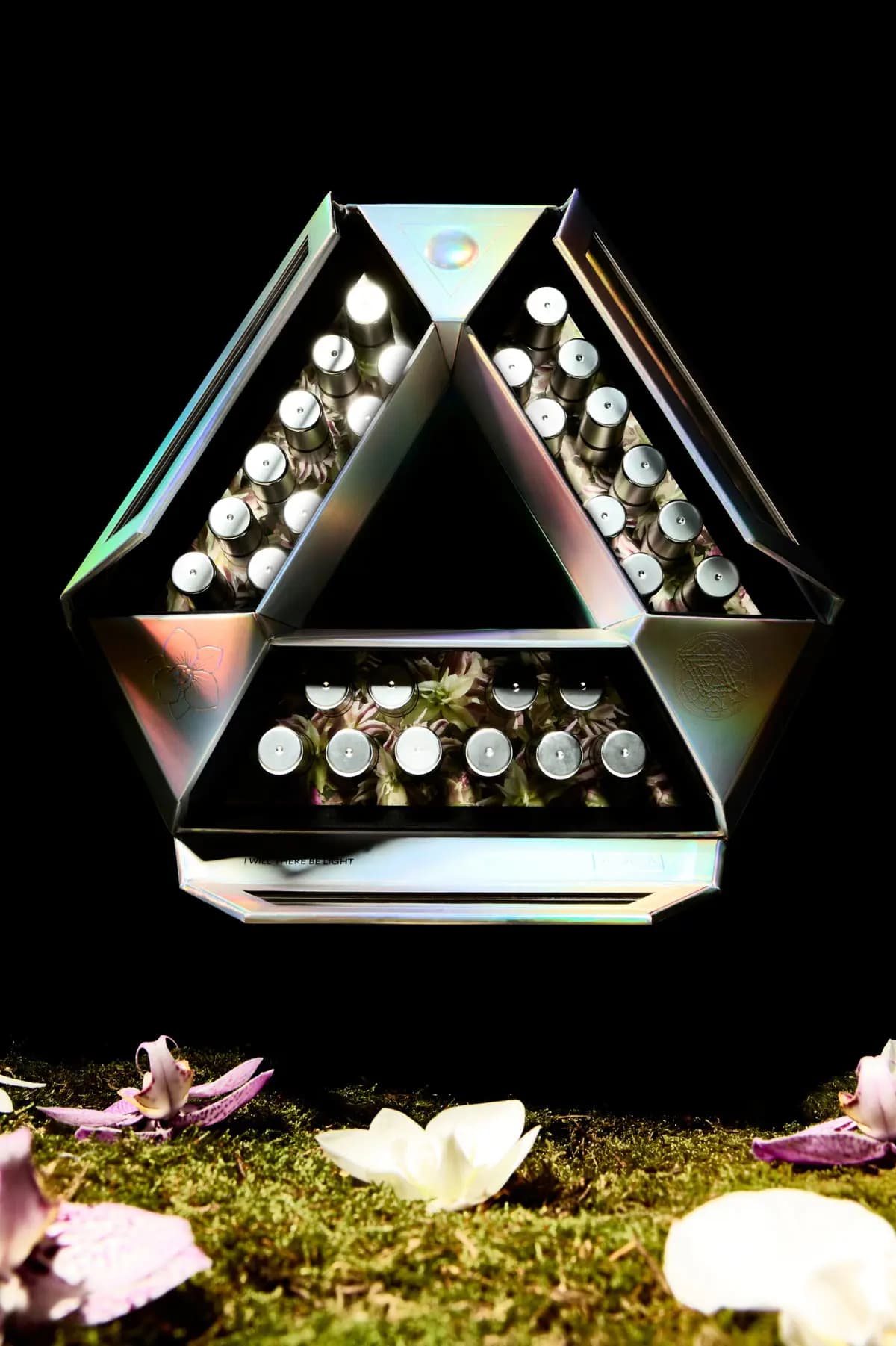 Open holographic triangle box of silver ampoules floating above moss scattered with pink and white orchid petals