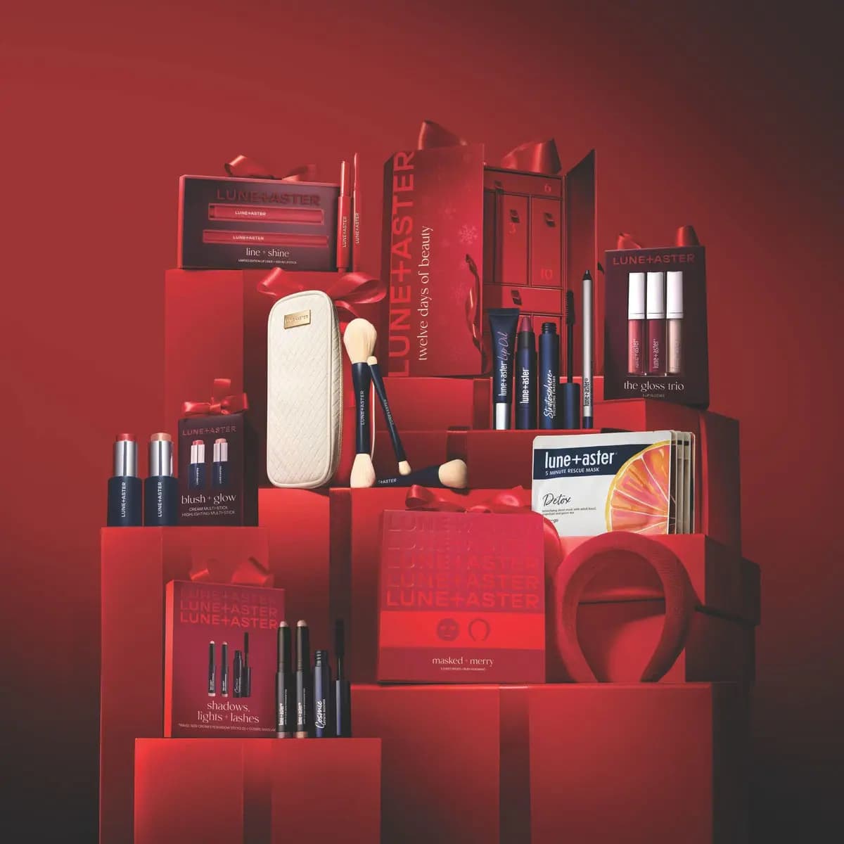 Lune+Aster holiday gift sets stacked on red ribbon-tied boxes, with advent calendar, brush case and red headband