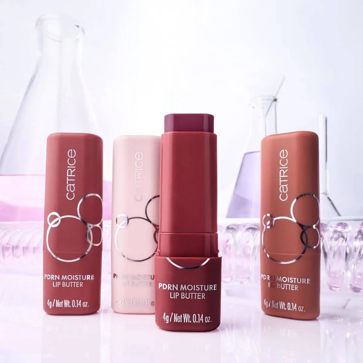 Four PDRN Moisture Lip Butter sticks in rose, nude pink, berry and caramel with lab glassware