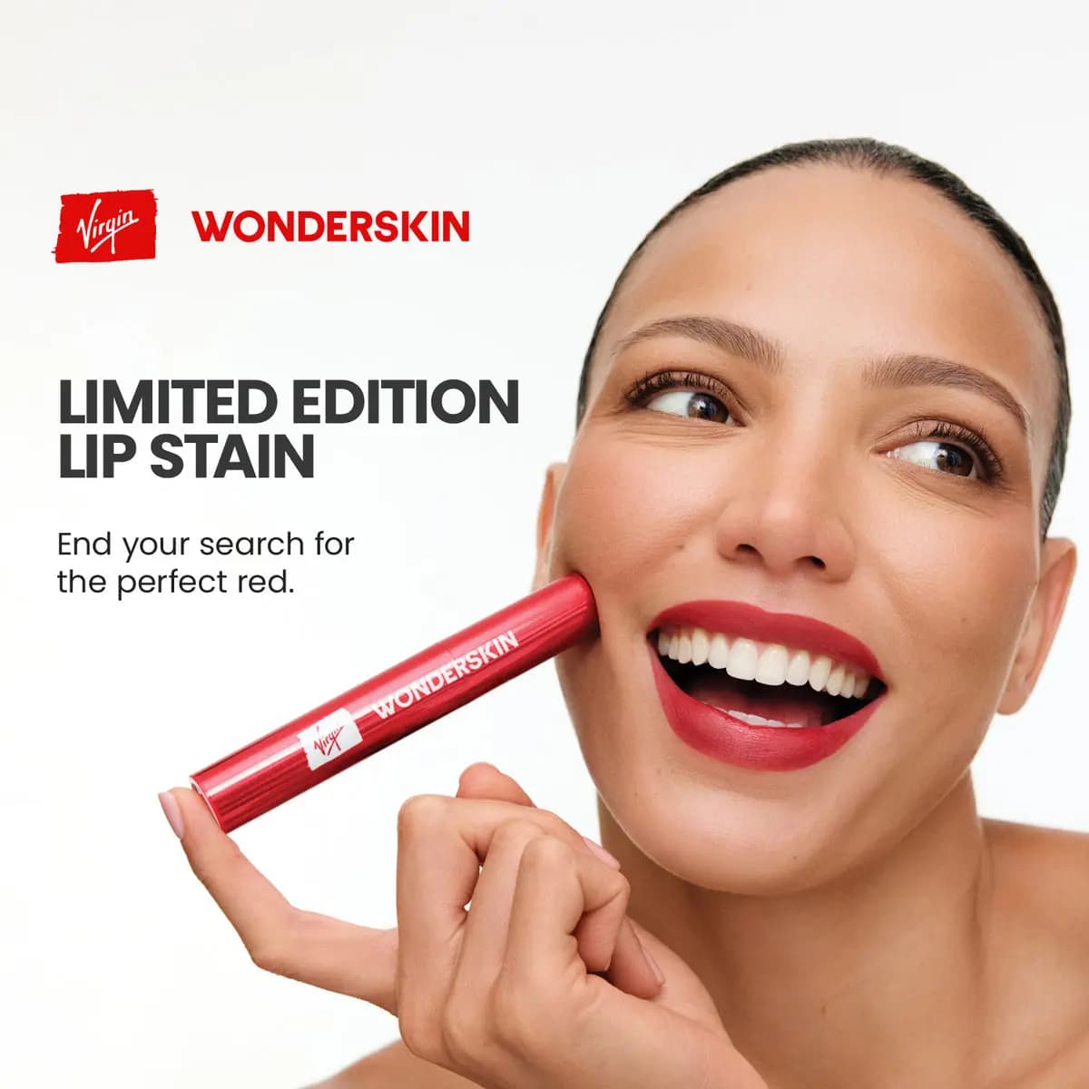 Smiling model with red lips holds a red metallic Wonderskin tube with Virgin logo against her cheek