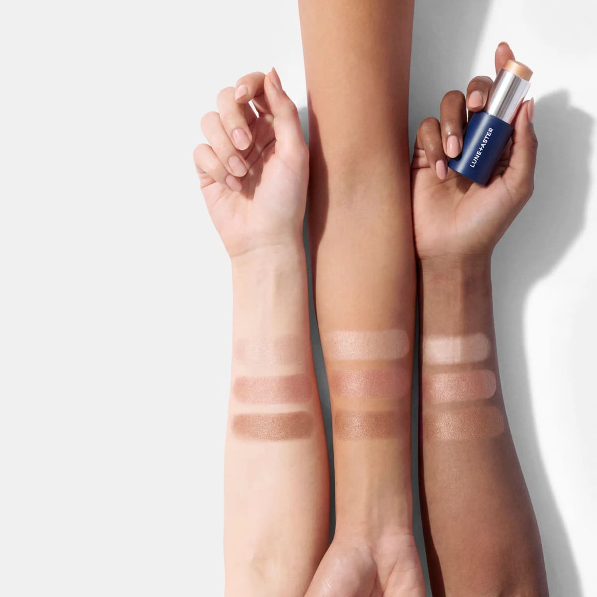 Highlighting Multi-Stick in three shades swatched on light, medium and deep arms, from pale pearl to bronze