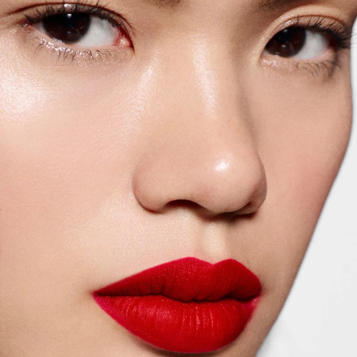 Close-up of a model with dewy skin wearing a bold, velvety matte red lip