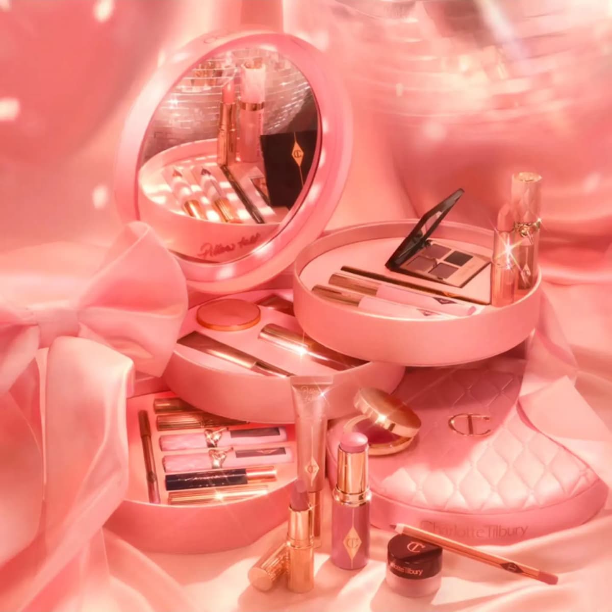 Dreamy pink-lit scene showing the open tiered vanity case revealing Pillow Talk products, with a compact, lipstick and bow