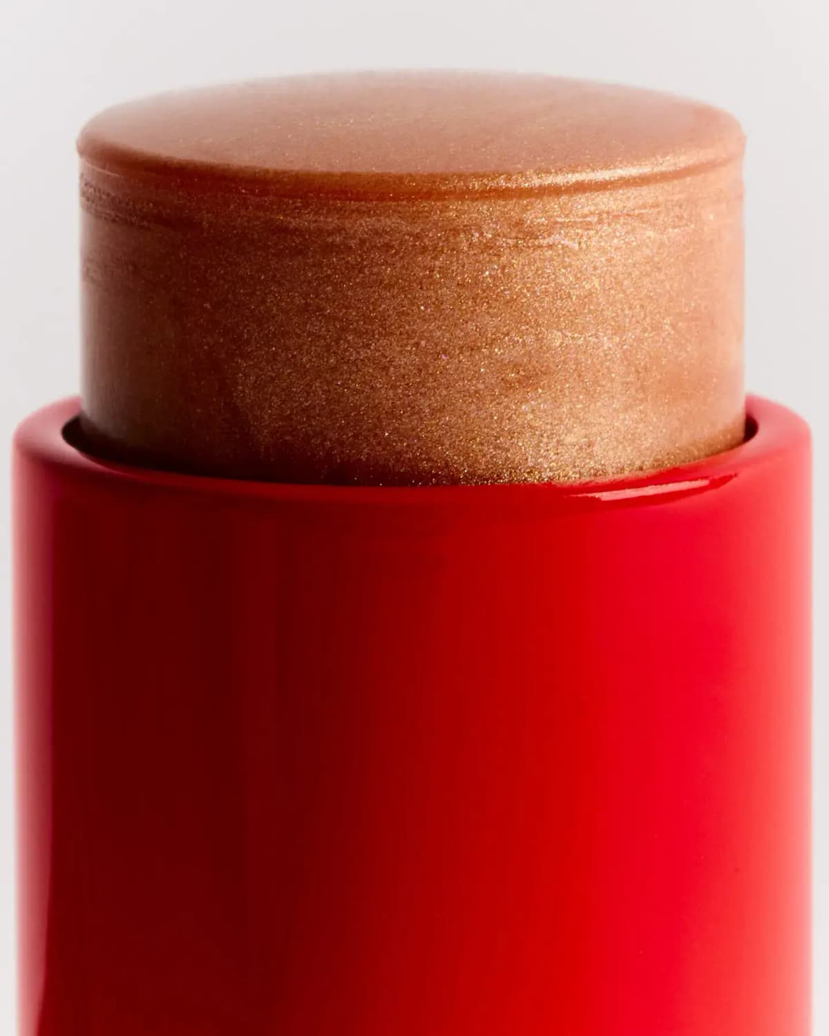 Close-up of the Shine Baume Stick's shimmering champagne-bronze balm rising from a glossy red tube