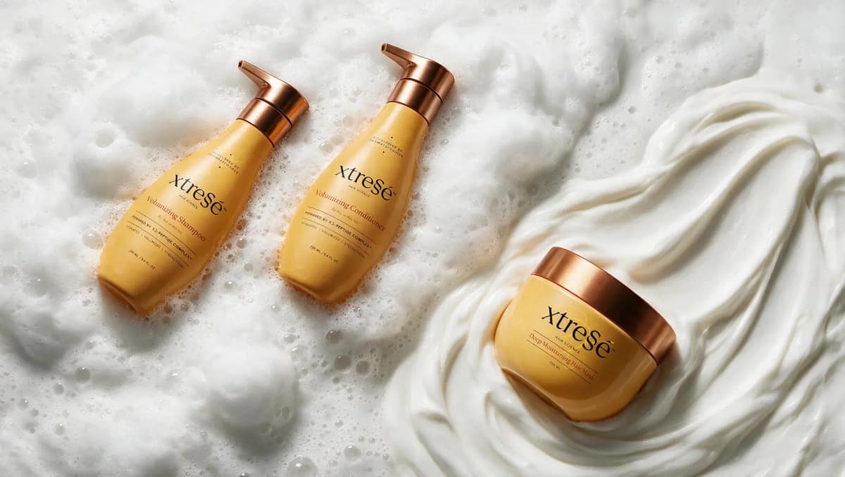 Volumizing Shampoo and Conditioner bottles lying in white foam next to a hair mask jar in swirled cream
