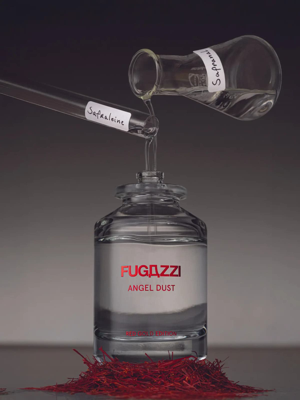 FUGAZZI Angel Dust Red Gold Edition bottle on a bed of red saffron threads, with lab glassware labelled Safraleine and Safranal pouring into it