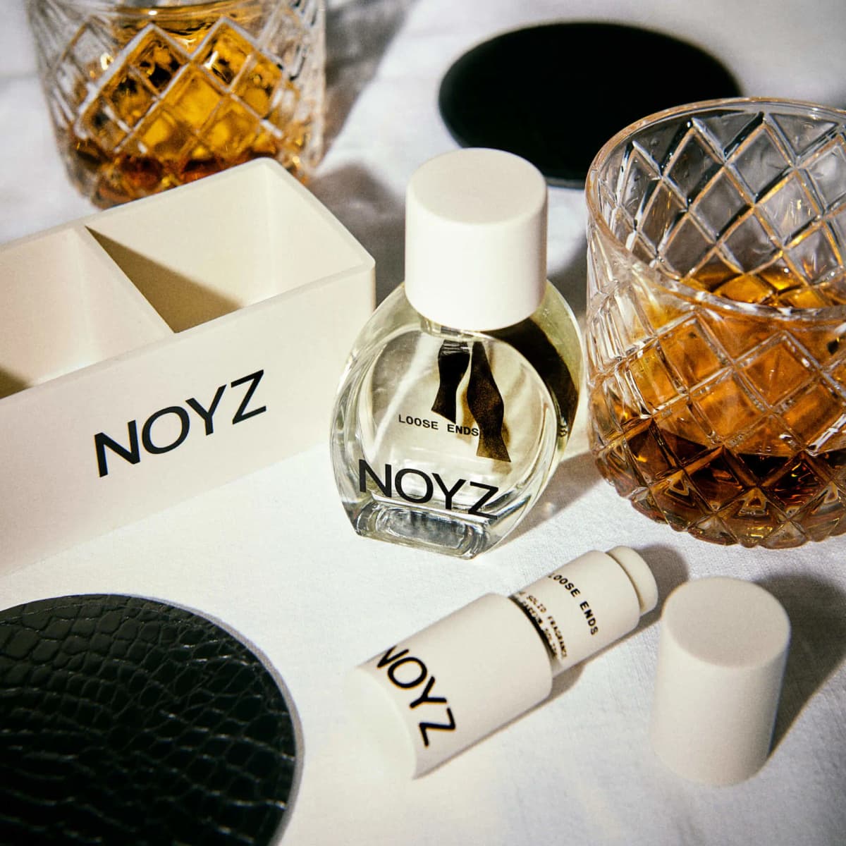 Loose Ends perfume and solid stick beside a NOYZ ice cube tray, croc coaster and cut-crystal glasses of whisky