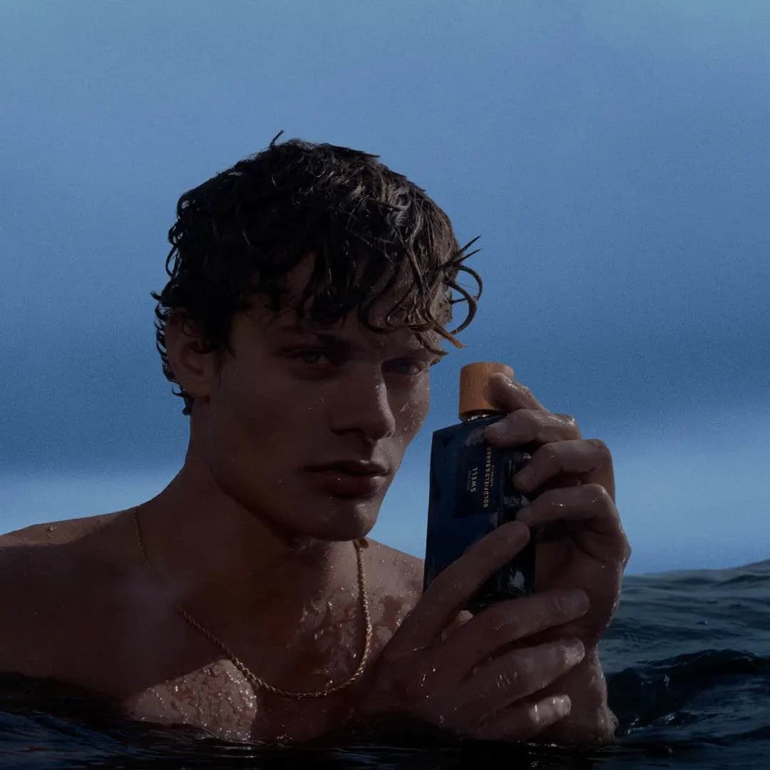 Wet-haired shirtless model in the sea holding the Pacific Rock Swell bottle up beside his face
