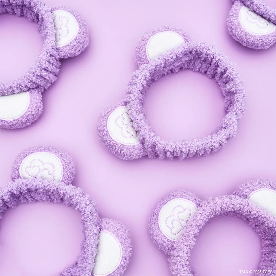 Purple fuzzy Care Bears headbands with bear ears and embroidered heart cloud patches on lilac background.