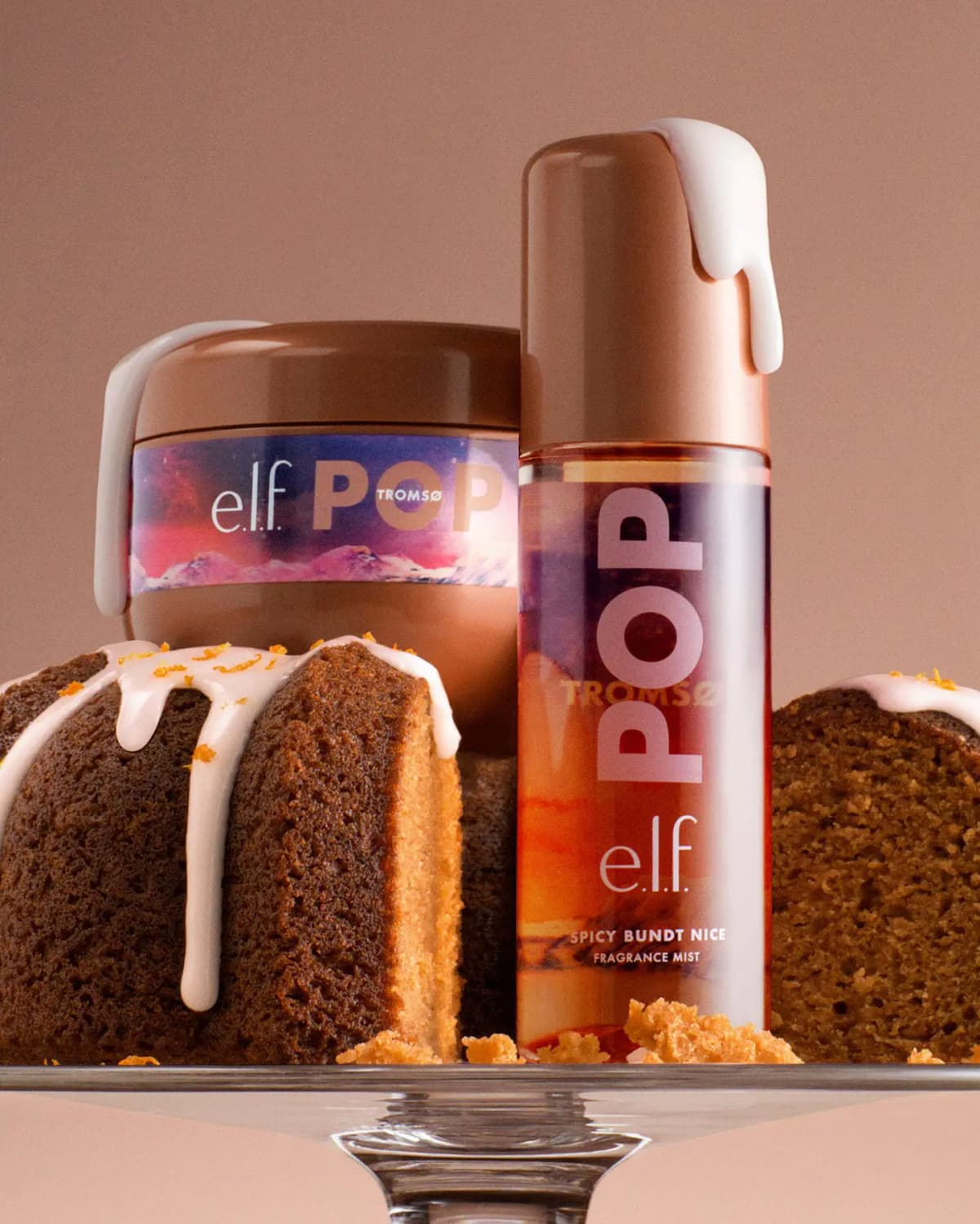 E.l.f. POP mist and body cream jar dripping with white icing, perched on a glazed spice Bundt cake on a glass stand.