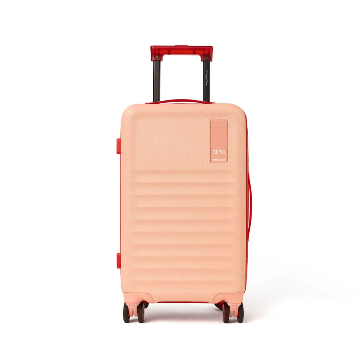 Front view of the peach hard-shell cabin bag with red handle, Tira x mokobara badge and four spinner wheels