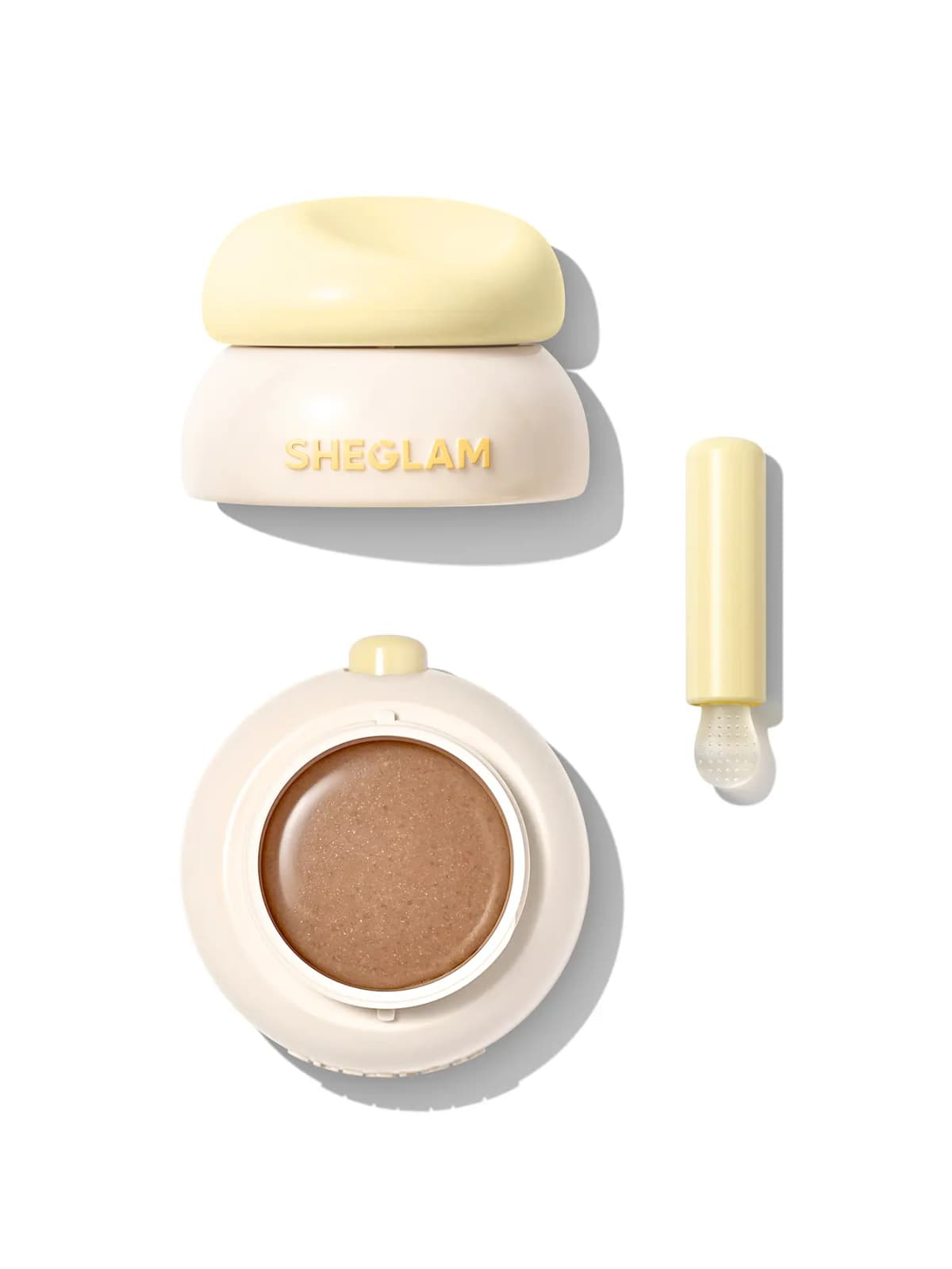 Cream jar with yellow lid, open pan of shimmery brown sugar lip scrub and yellow textured applicator on white