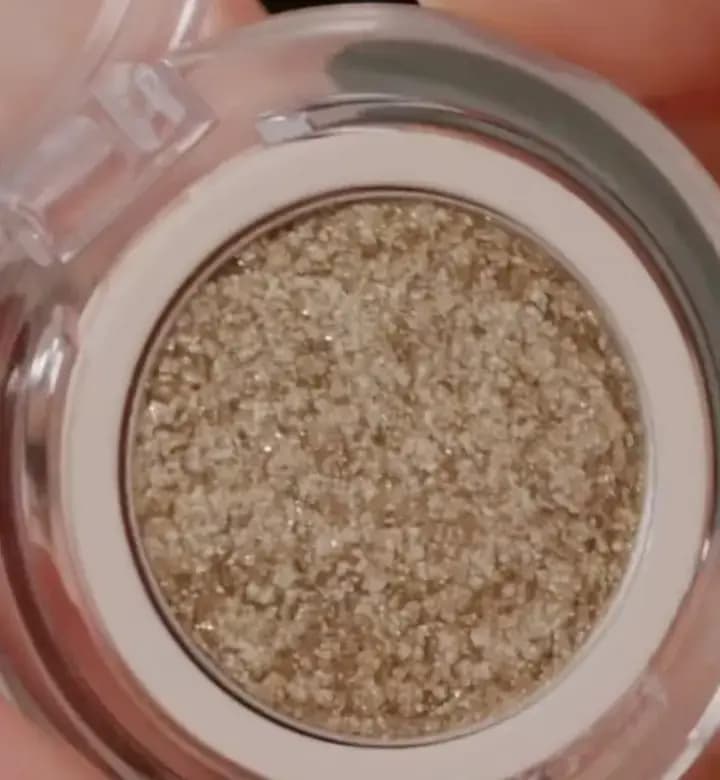 Close-up of a golden glitter pressed eye topper in its pan, showing chunky sparkly flakes