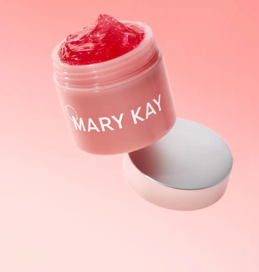 Open pink Mary Kay jar of red gel tilting above its silver lid on a soft coral pink gradient