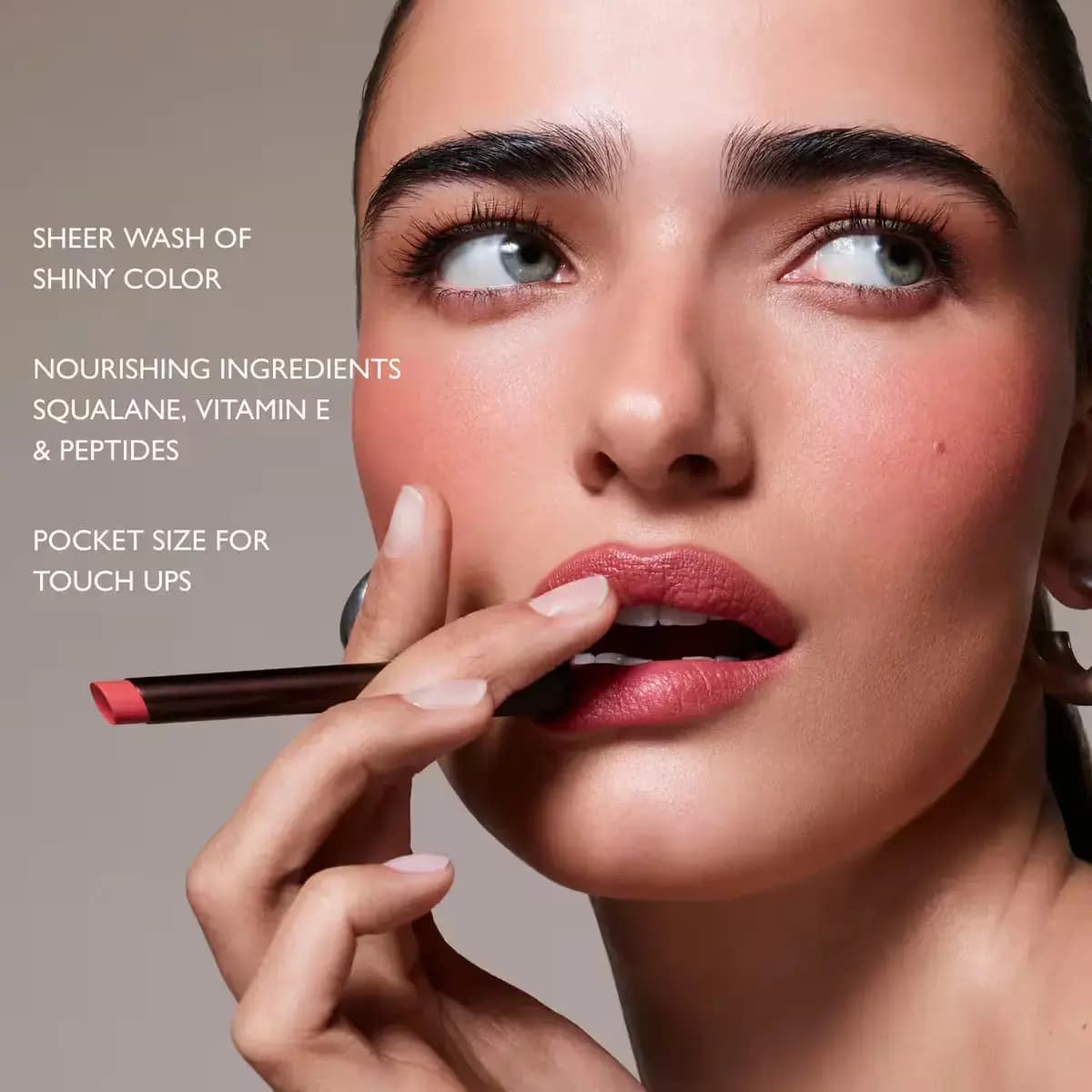 Model holding a coral Lip Ciggy to her rosy lips with text on sheer shine, squalane, vitamin E and peptides