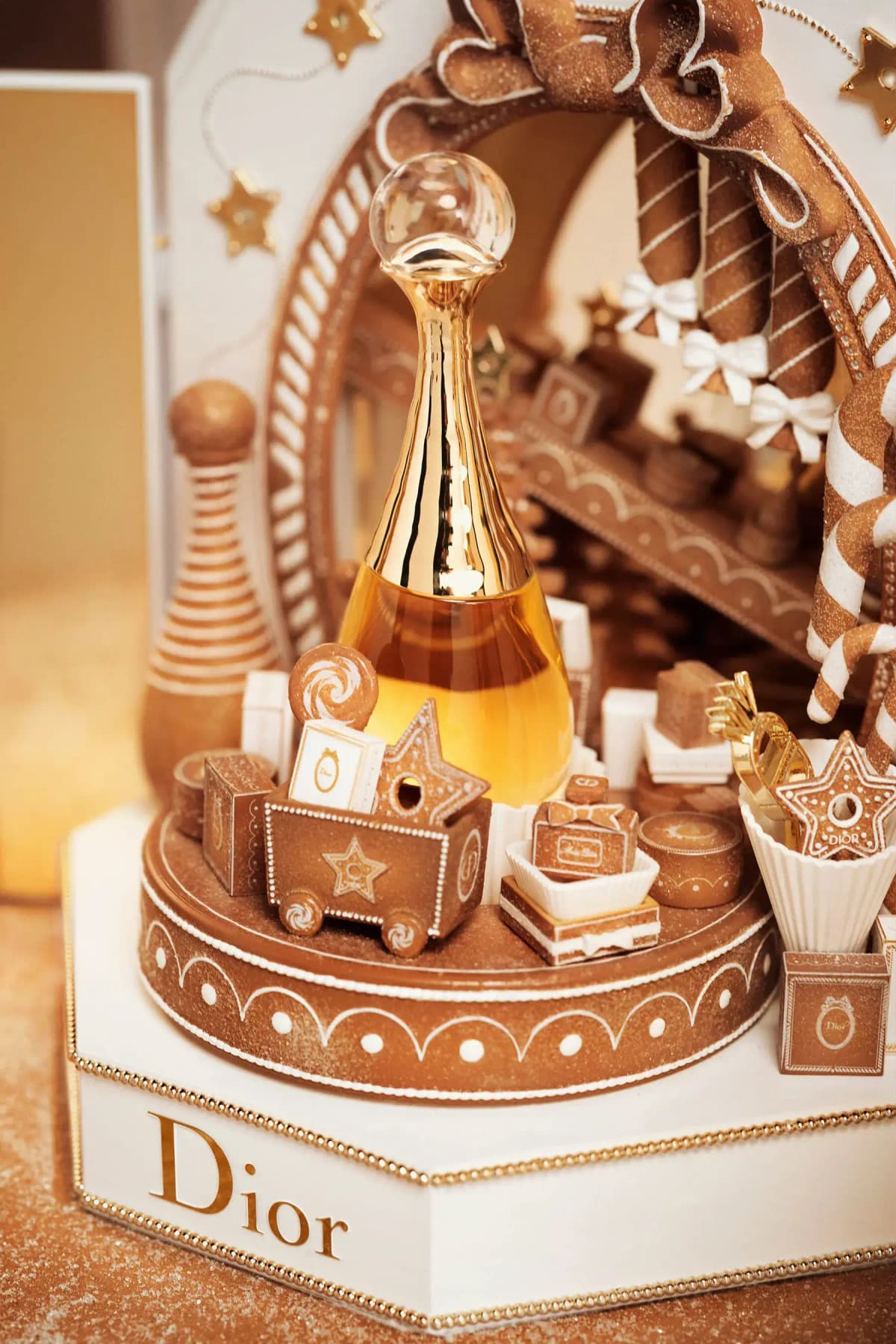 Close-up of the gold-necked J'adore bottle among miniature gingerbread gifts, star cookies and candy canes on the turntable