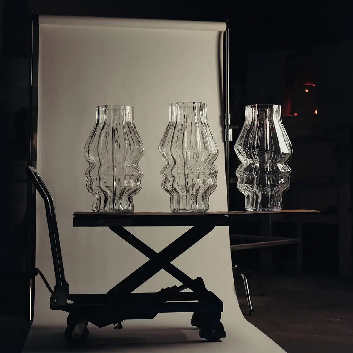 Three rippled clear glass hurricanes on a scissor-lift cart against a white paper backdrop