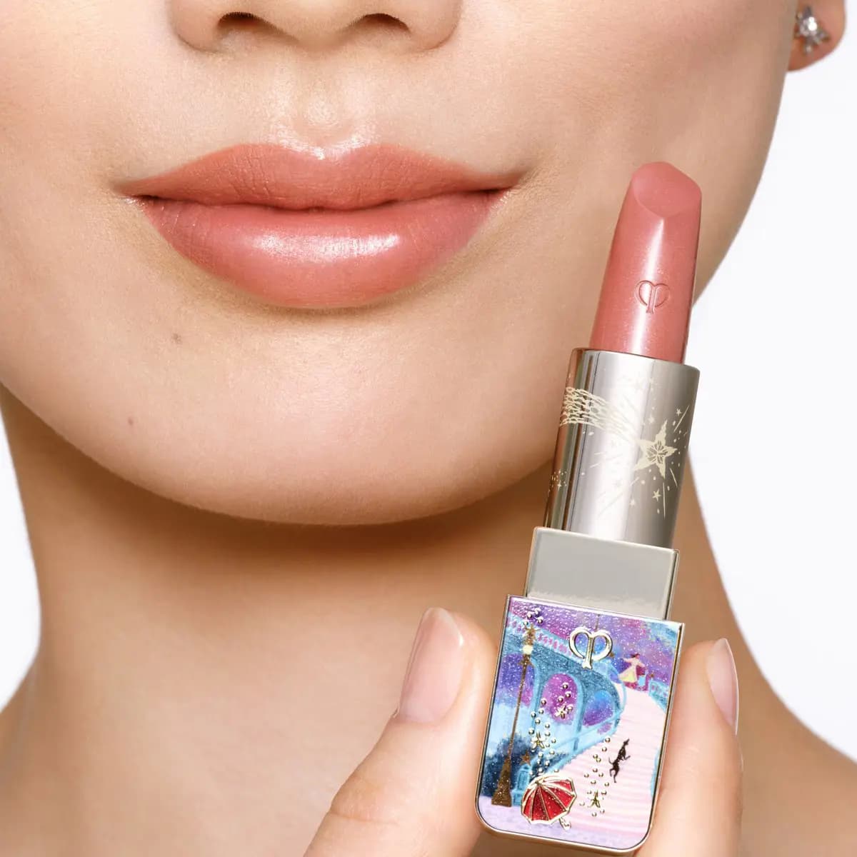 Close-up of lips in a glossy peachy-nude shade beside the illustrated limited-edition lipstick held in hand