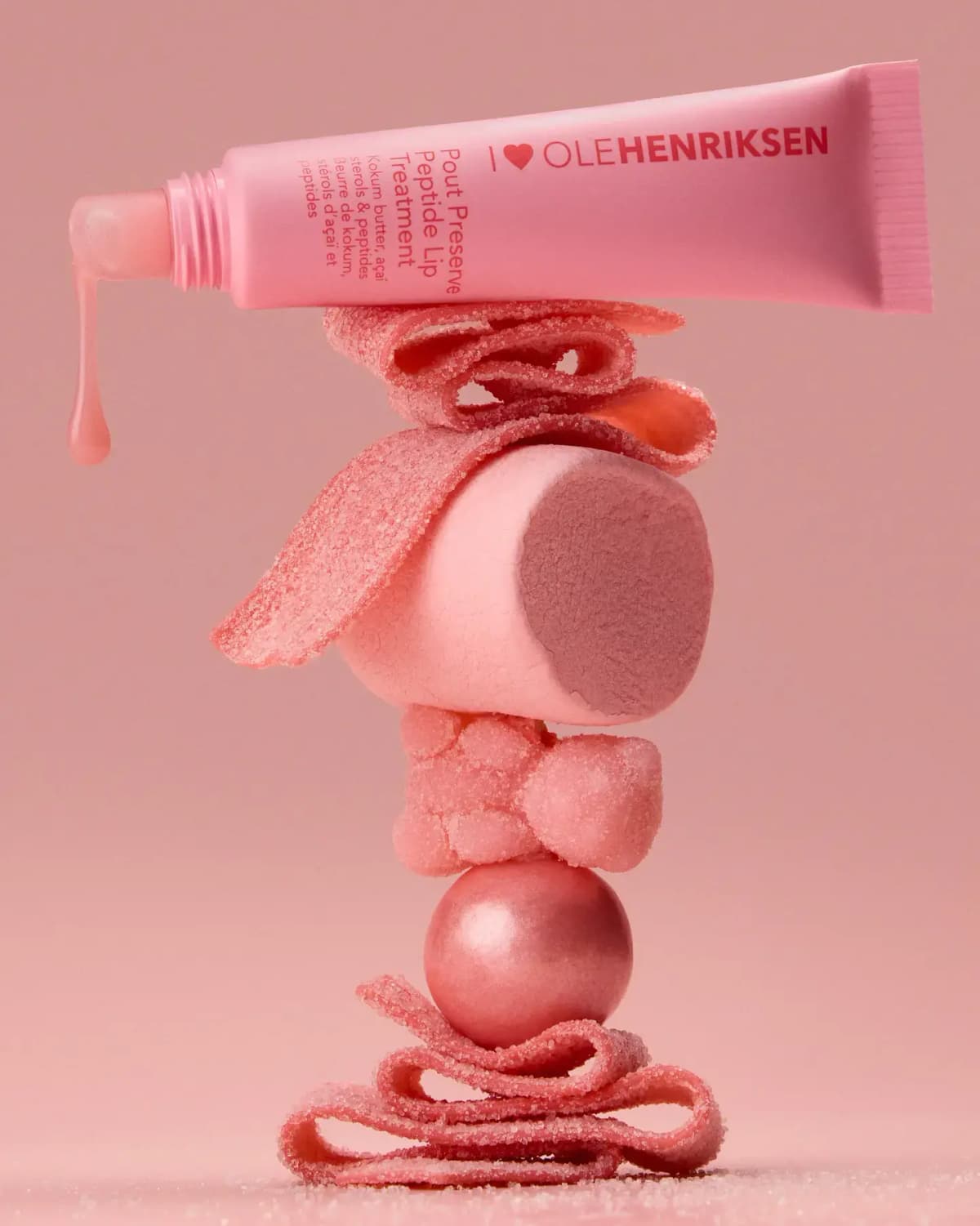 OLEHENRIKSEN Pout Preserve Peptide Lip Treatment in Scandi Candy, pink tube dripping gloss atop stacked pink sugared candies