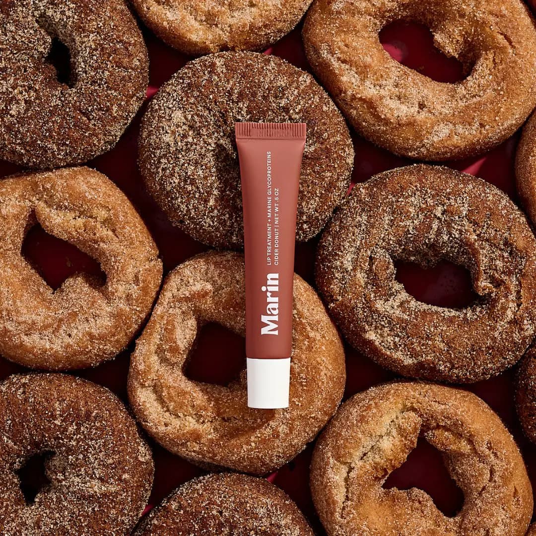 Marin Cider Donut Lip Treatment tube lying on a pile of cinnamon-sugar cider donuts