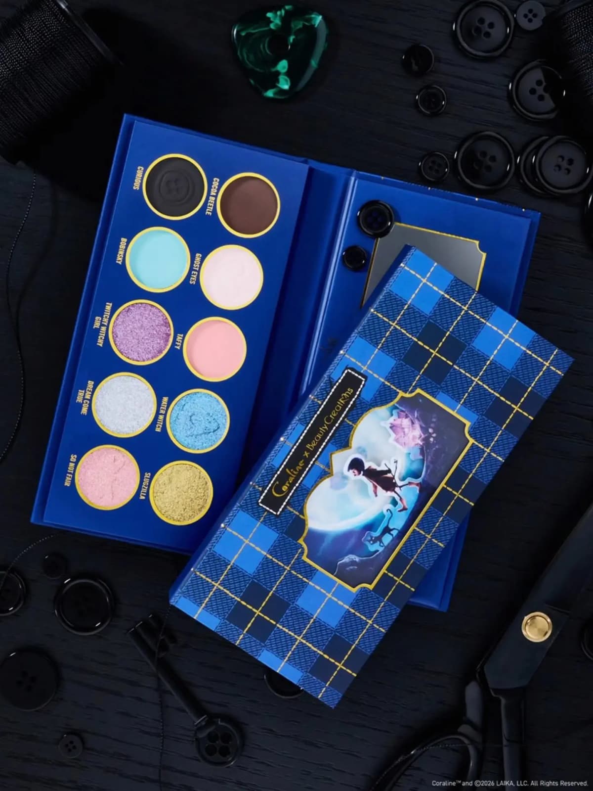 Open blue plaid eyeshadow palette with 10 shades including Curious, Cocoa Beetle, Bobinsky and Sluqzilla, surrounded by
