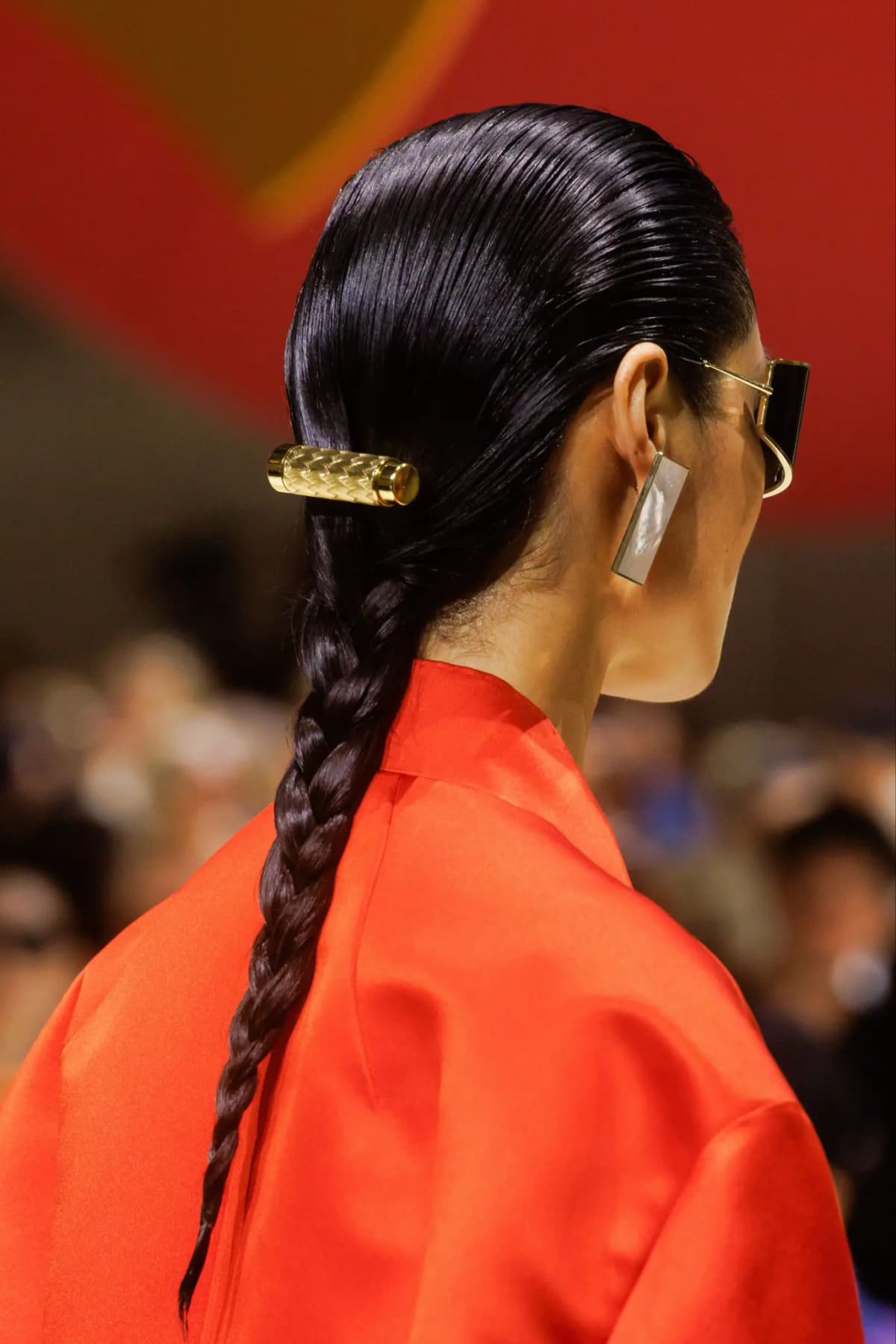 Woven-texture gold lipstick clip in a slick braided ponytail, worn with a red satin top and mirrored earring