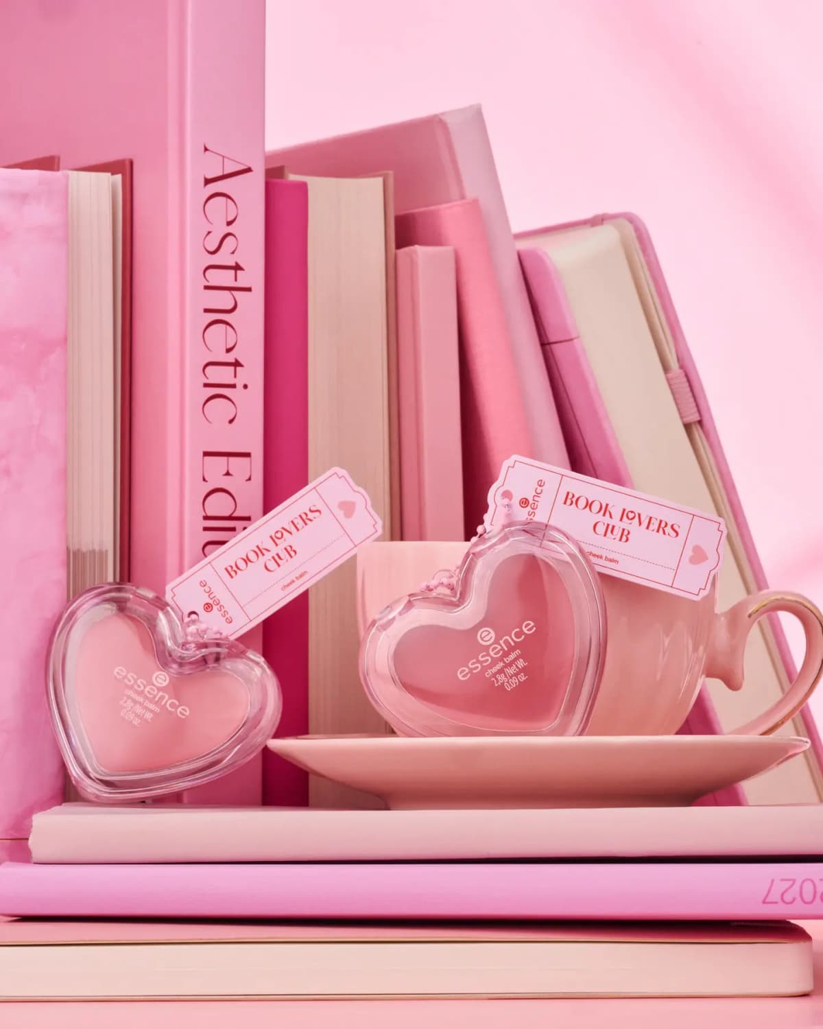 Two heart-shaped cheek balm compacts with Book Lovers Club ticket tags among pink books and a teacup