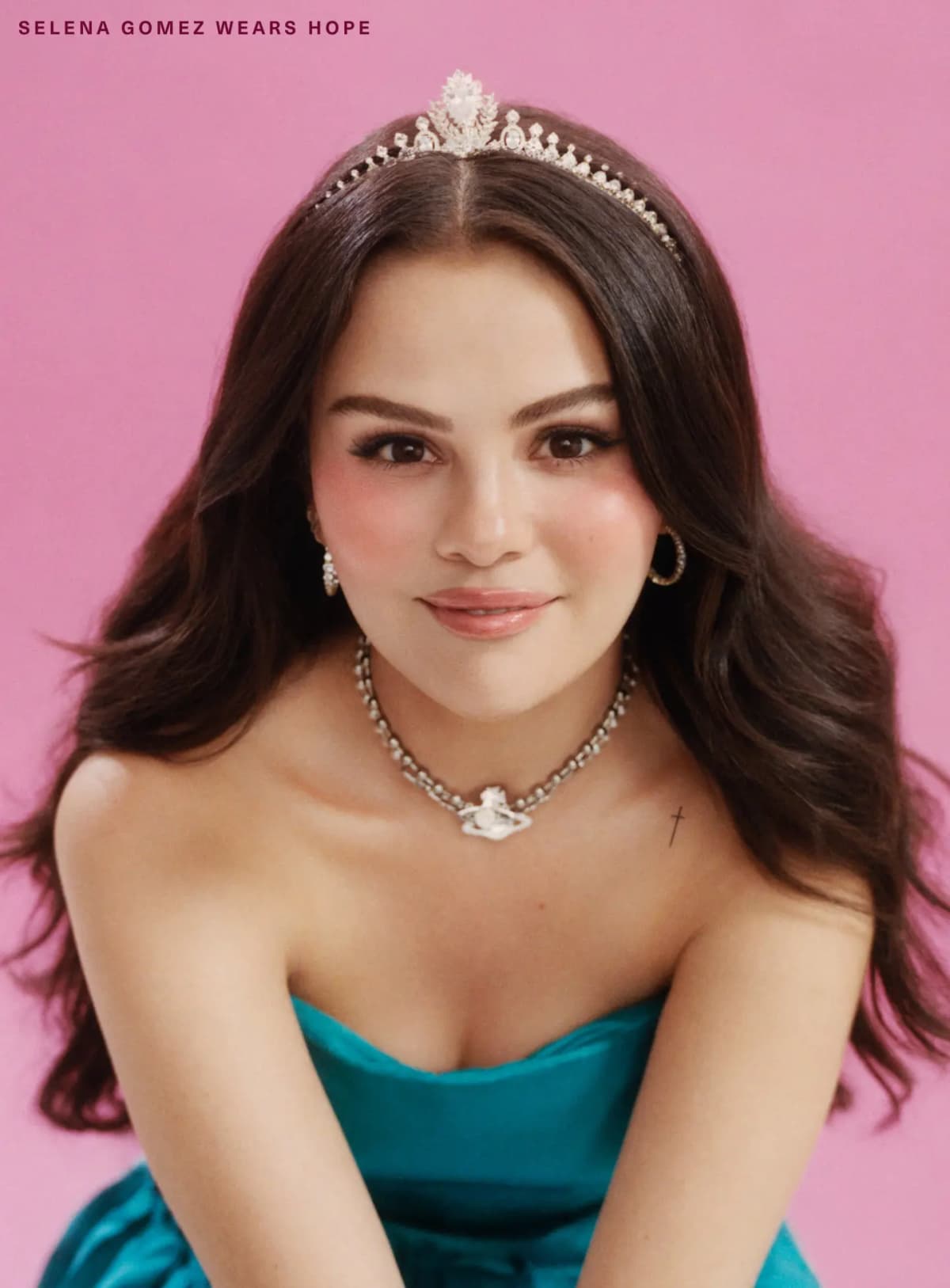 Selena Gomez wearing Hope blush, in a tiara and teal strapless dress against a pink backdrop