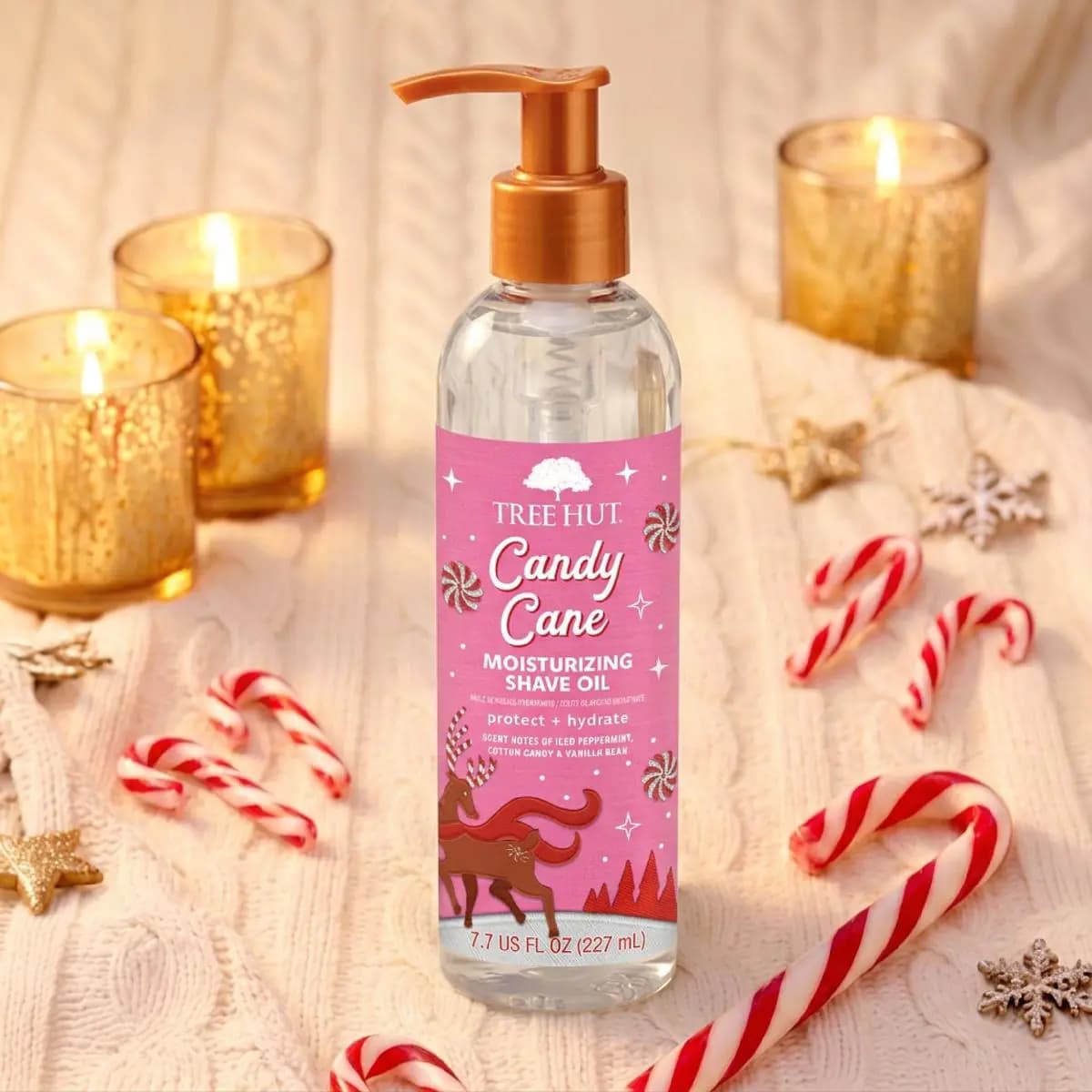Tall clear pump bottle of Candy Cane Moisturizing Shave Oil surrounded by candy canes, gold candles, and snowflake decor