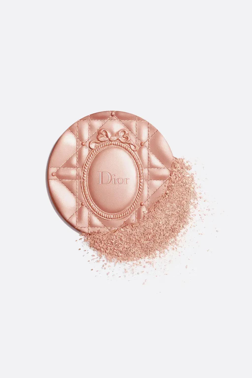 Shimmering rosy-peach Dior highlighter pan with Cannage and bow medallion relief beside a pile of crushed powder
