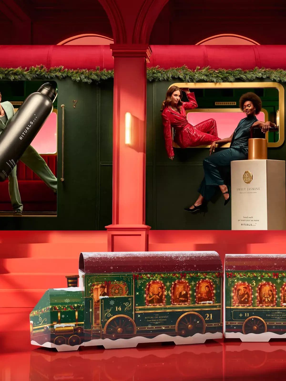 Train calendar on a red floor below models posing in a green carriage with giant Sweet Jasmine hand wash and black bottle