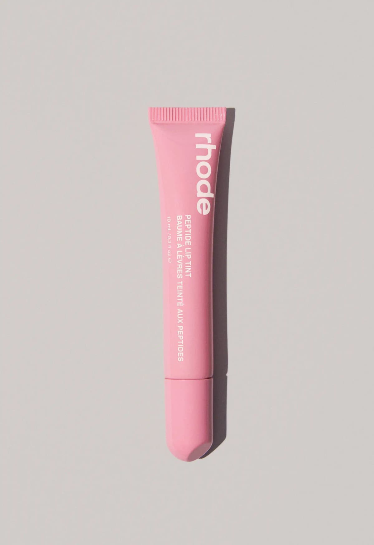 Bubblegum-pink rhode Peptide Lip Tint tube with white branding set against a pale grey backdrop