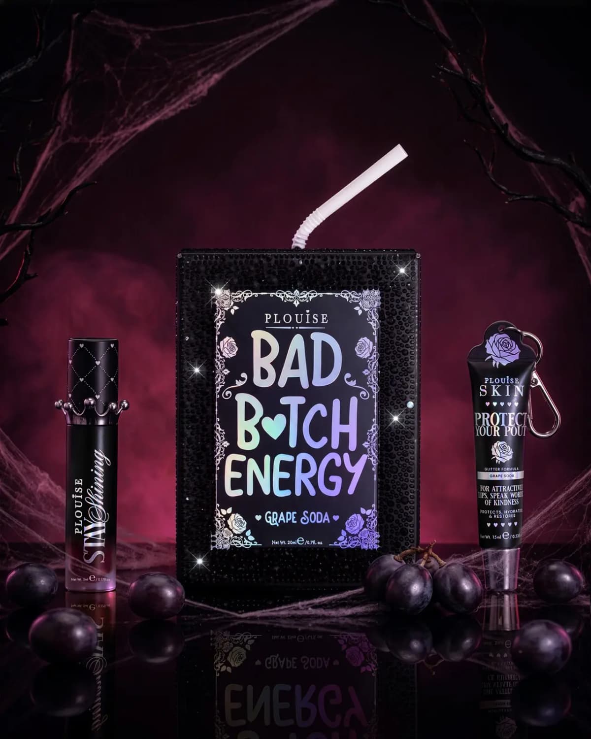 Grape Soda Bad B*tch Energy set in a black rhinestone box with lip oil and rose lip balm keyring among grapes