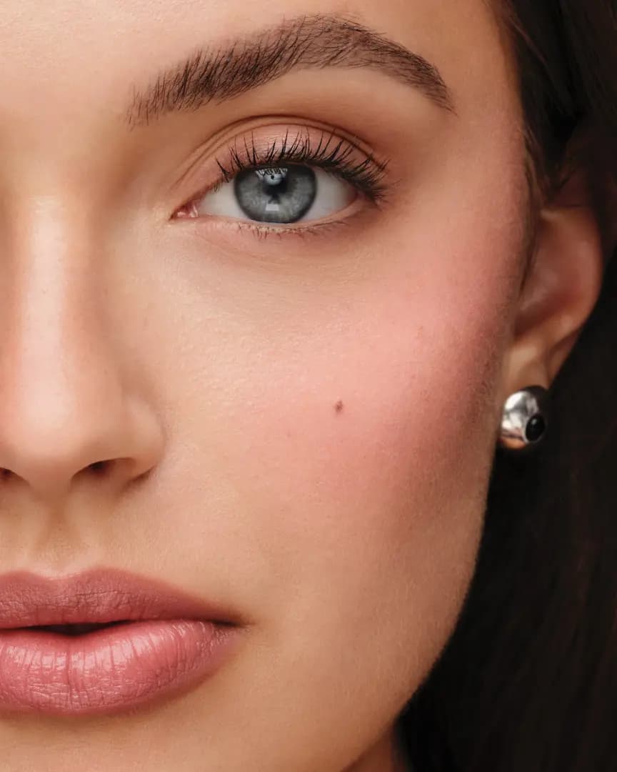 Close-up of a grey-eyed model wearing soft neutral eyeshadow, flushed pink cheek, nude lip and silver stud earring