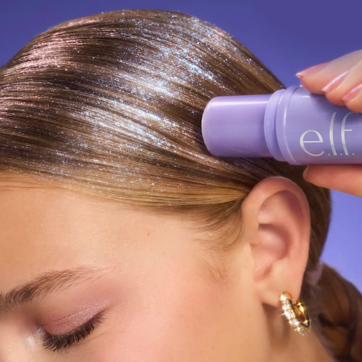 Close-up of a model applying glitter stick to her sleek brown center-parted hair, showing sparkling shine.