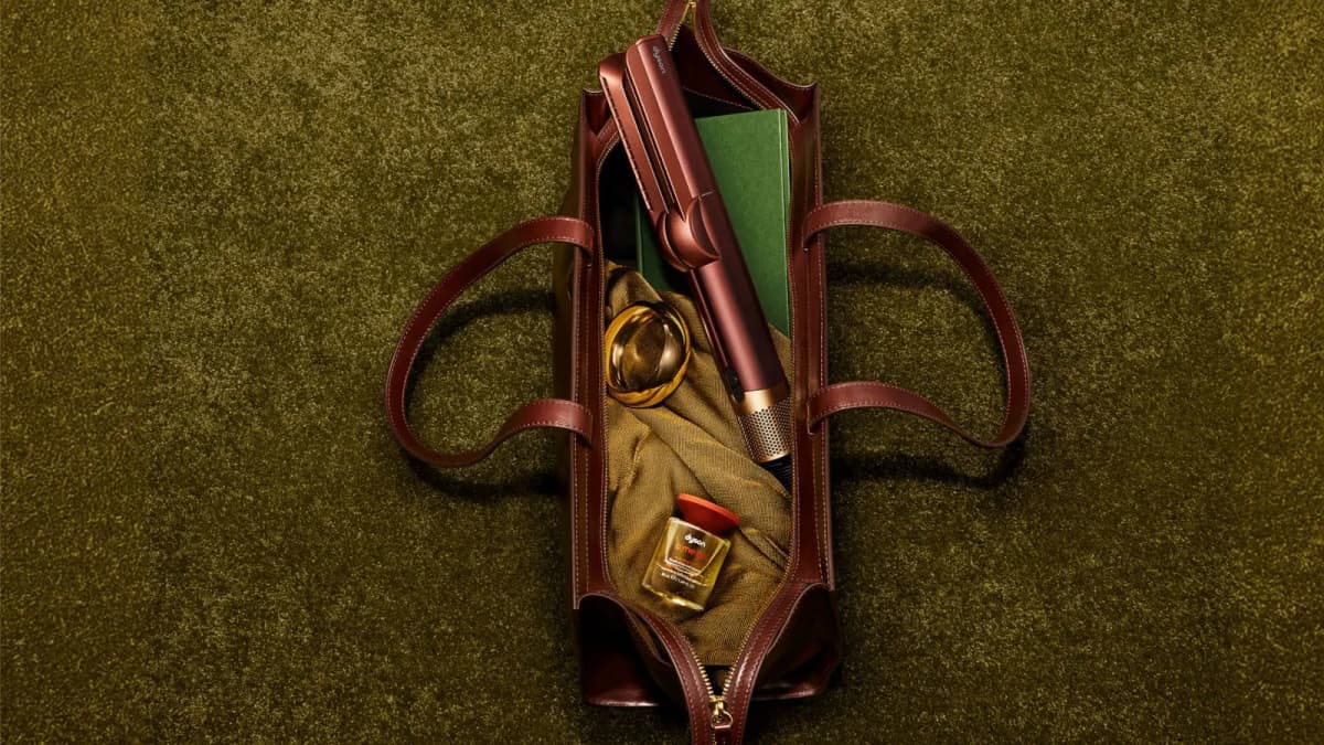Copper hair straightener inside a brown leather tote with a green book, gold bangle and a Dyson oil bottle