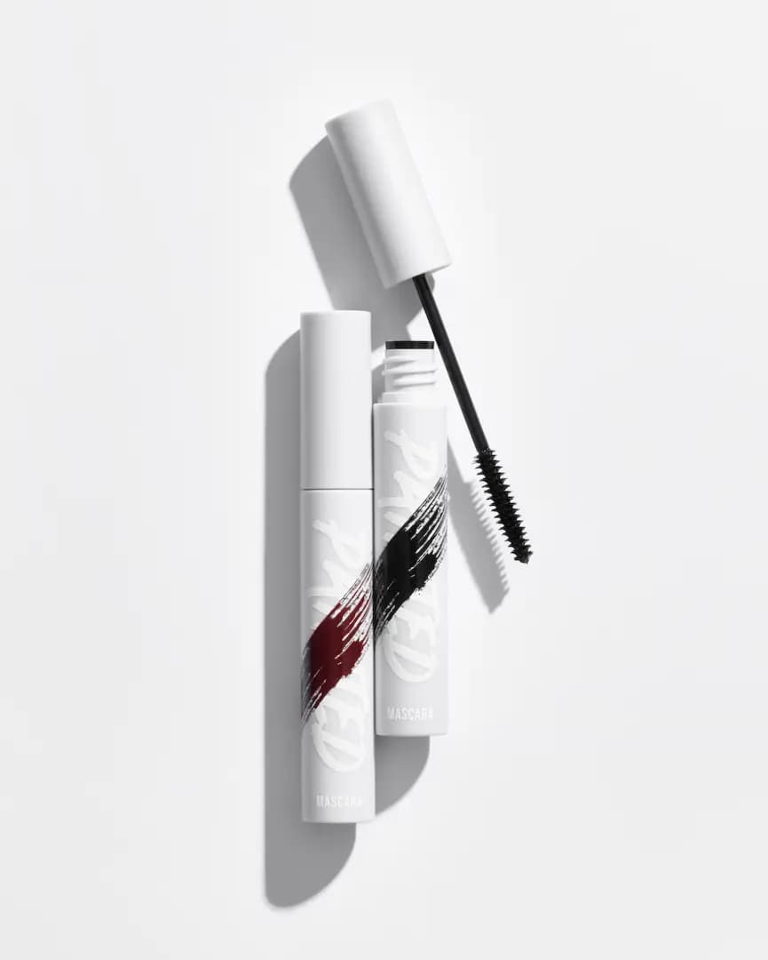 Painted Mascara tubes in white with brown and black brush-stroke graphics, one open with its black spoolie wand