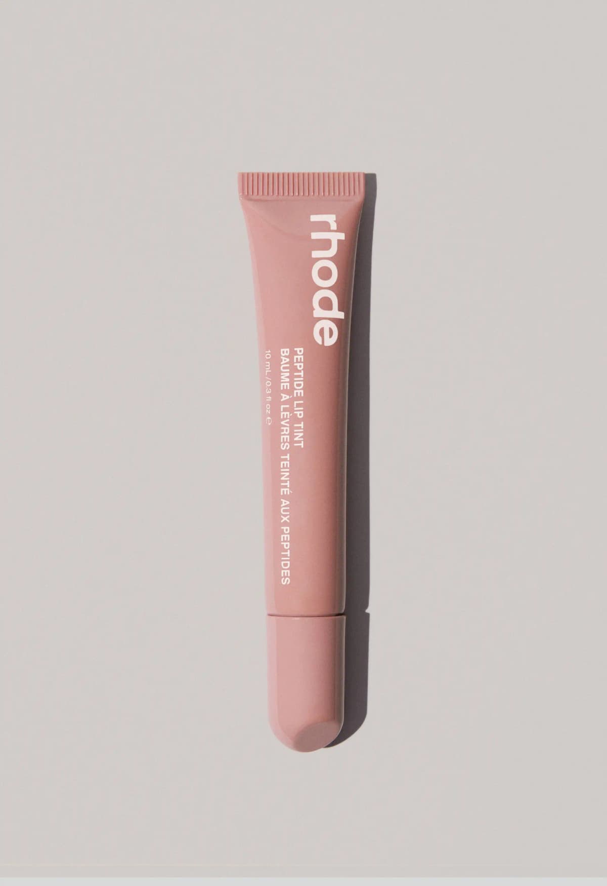 Dusty nude-pink rhode lip tint tube with a slanted cap, photographed on a light grey background