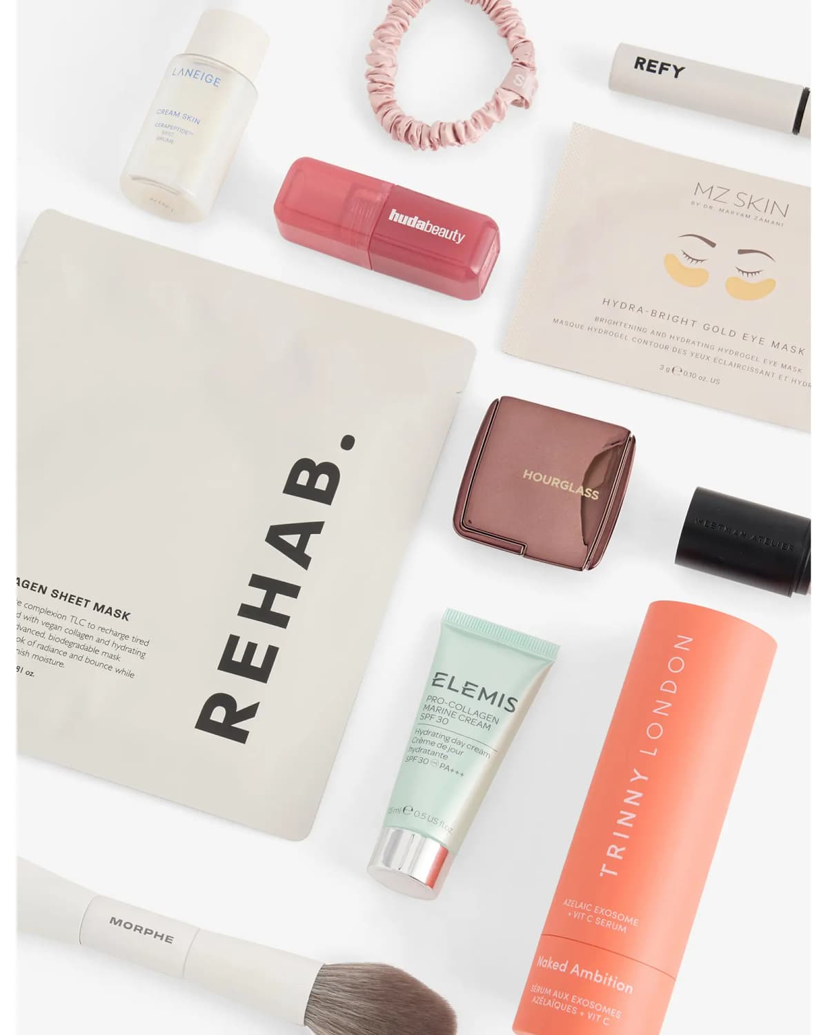 Flat lay of Laneige mist, Huda Beauty blush, Rehab mask, MZ Skin eye mask, Hourglass compact, Elemis cream