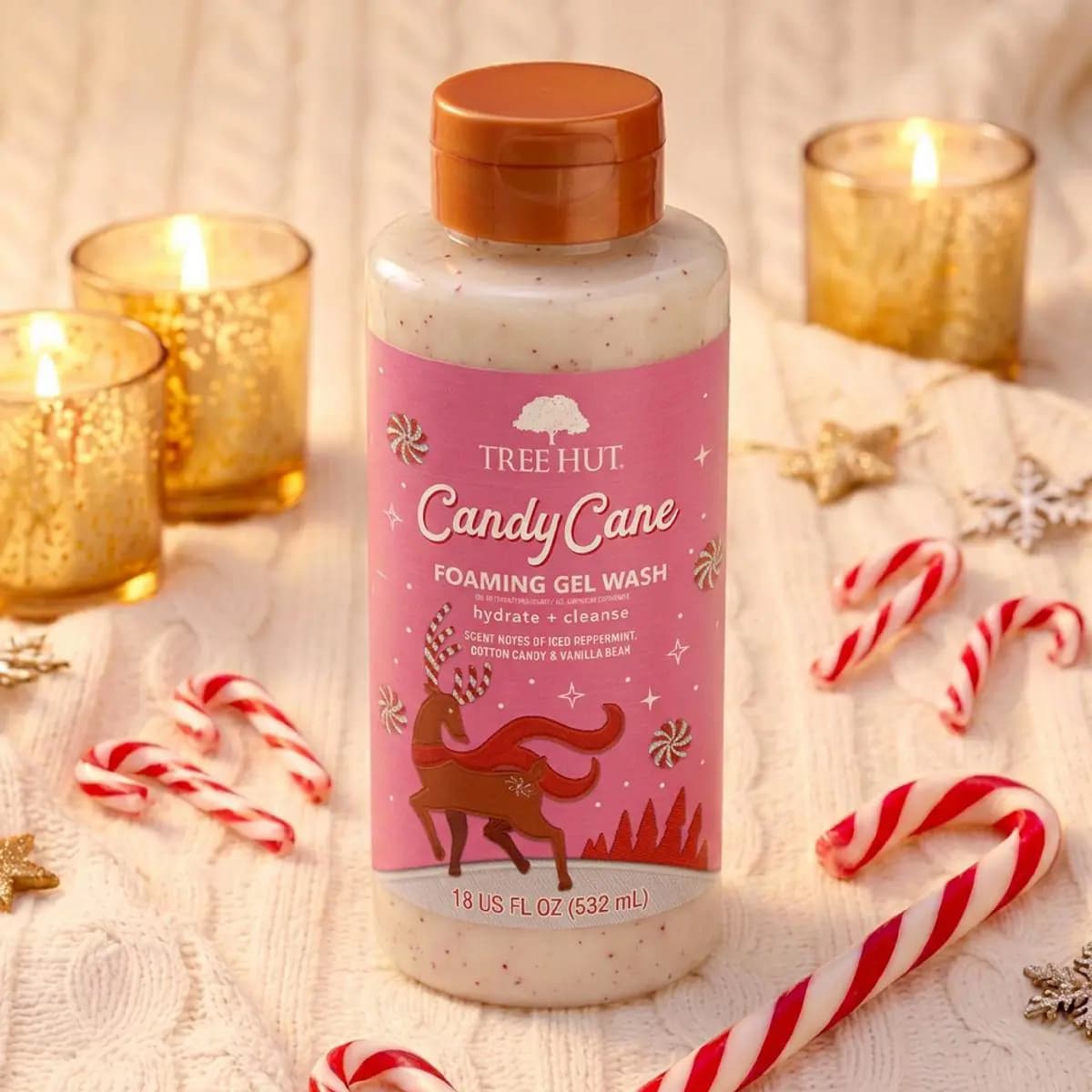 Candy Cane Foaming Gel Wash bottle with speckled cream liquid, candy canes, and glowing gold votives on knit