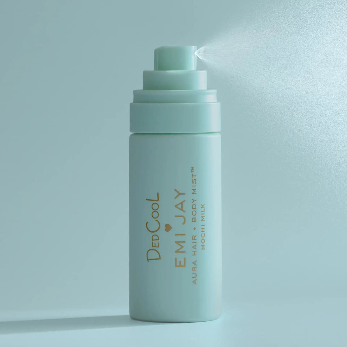 Mint DedCool x Emi Jay mist bottle releasing a fine spray against a soft aqua background