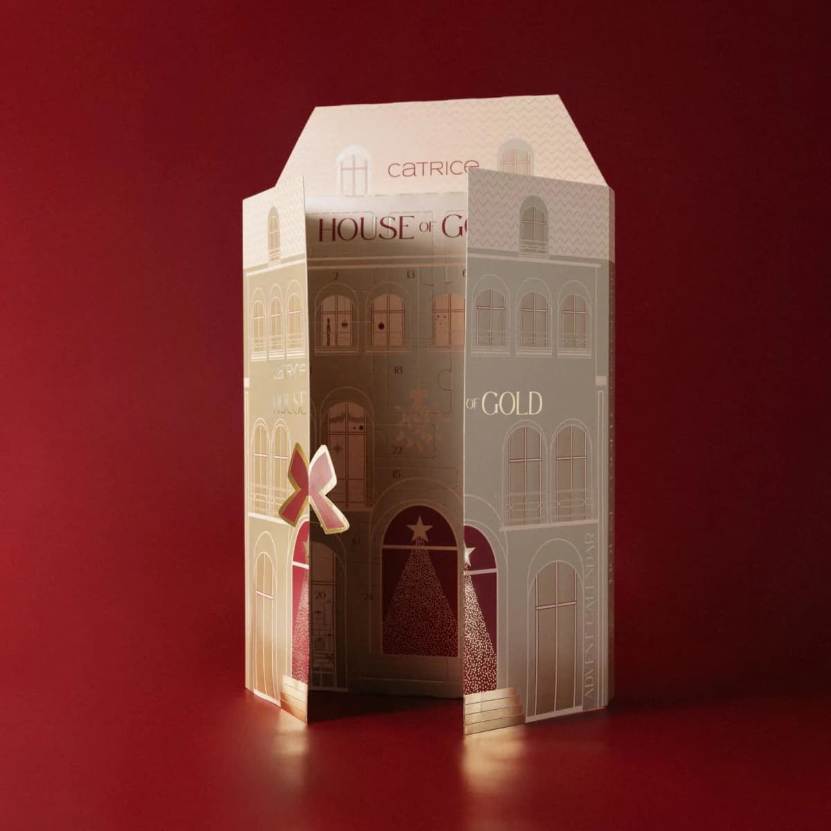 Catrice House of Gold advent calendar standing partly open on a red backdrop, its cream and gold doors folded outward