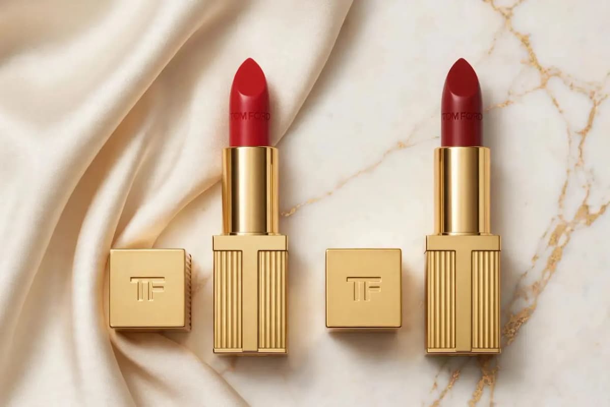 Two gold Tom Ford lipsticks, bright red and deep red, beside TF caps on cream satin and gold-veined marble