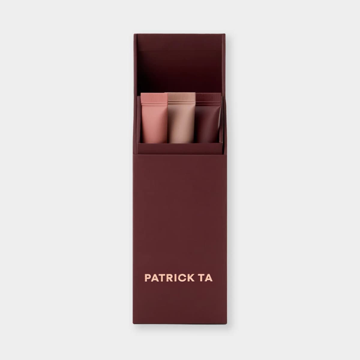 Burgundy box holding three lip balm tubes in peachy rose, beige nude and deep plum