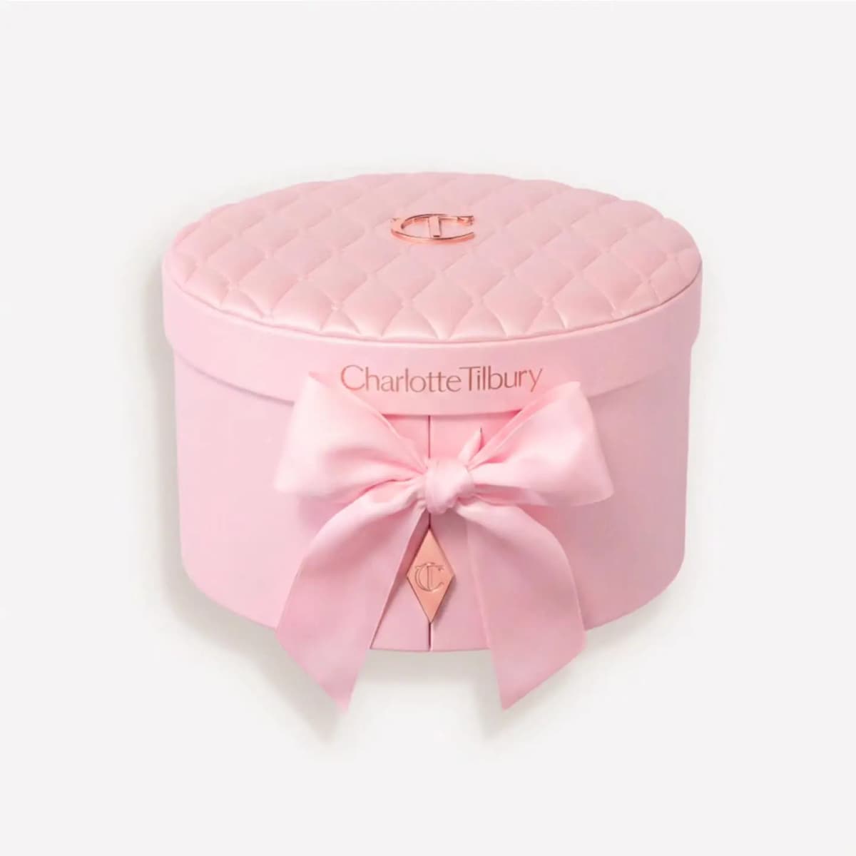 Round quilted pink vanity case with rose-gold CT emblem and satin pink bow tied at the front.