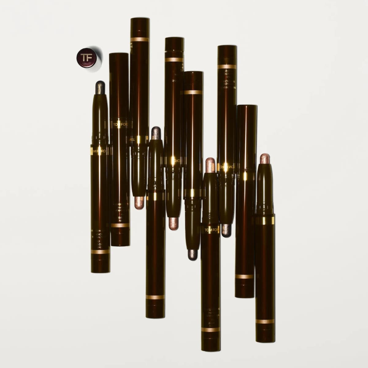 Dark brown Eye Color Stylo pens with gold bands arranged diagonally, some uncapped showing bronze, rose and taupe tips