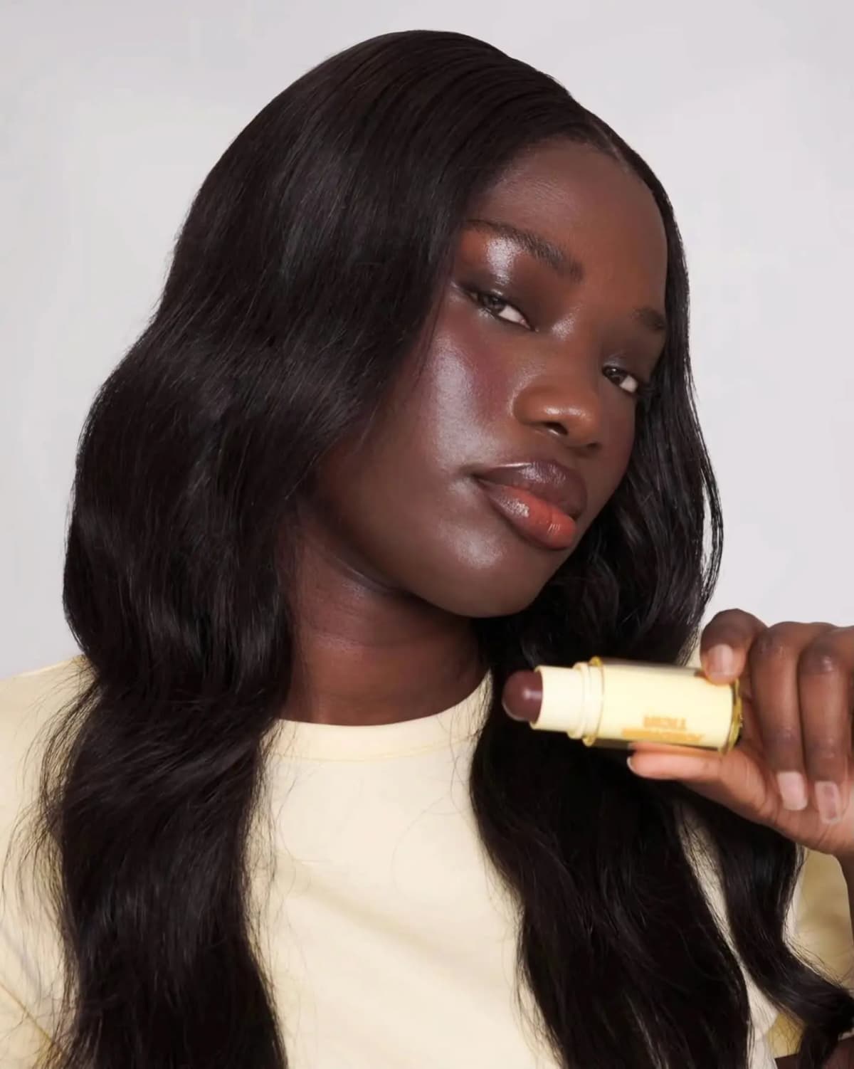 Model with deep skin and long dark hair holds an open stick with a deep brown bullet